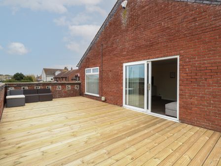 A large wooden deck attached to a brick building with sliding doors and outdoor seating at The Look Out in Sea Palling