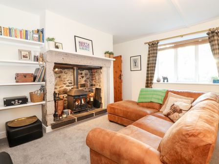 A living room with a leather sofa wood burning stove and shelves with books at Garden Cottage in Chathill near Beadnell