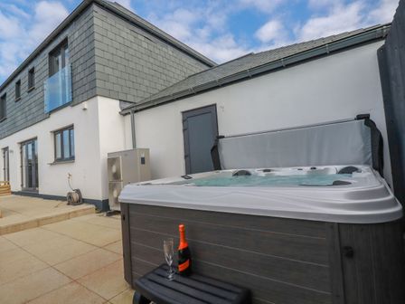 An outdoor patio area with a hot tub and a bottle of champagne with glasses at Lavender House in Crantock