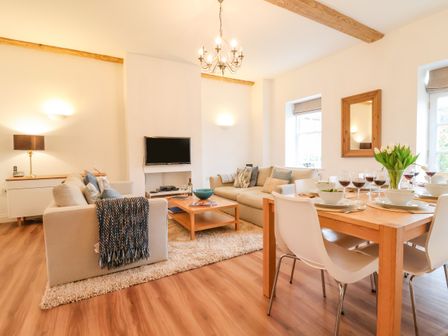 A living room with beige sofas wooden coffee table wall mounted tv and dining table set with wine glasses and tulips at Feathers Blythburgh in Reydon