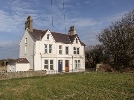 A two-story white house with two chimneys and front doors facing a grassy area at Gwynant - Morfa Nefyn in Morfa Nefyn
