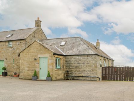 Stone cottage building with green door and windows by a brown wooden fence at The Byre Longwitton near Morpeth
