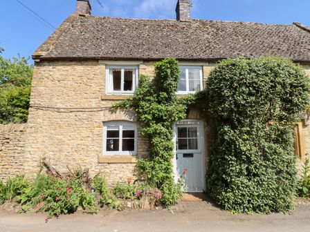 A stone cottage with green climbing plants around the door and windows at Woodbine Cottage in Donnington near Stow-On-The-Wold