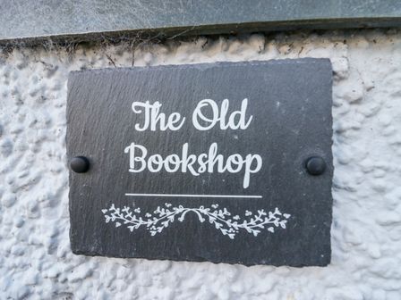 A black plaque with the text The Old Bookshop mounted on a white textured wall at The Old Book Shop in Cartmel