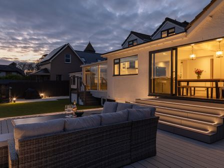 An outdoor seating area with a sofa and a table with wine glasses outside a house with lit stairs at Sou West in Hope Cove