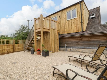 An outdoor area with wooden stairs leading to an upper floor and lounge chairs on gravel at The Attic at Redmond Bottom in Wookey