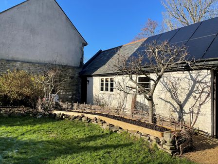 A garden with leafless trees and a small fence next to a stone and white brick building with solar panels on the roof at Carnotze in Owermoigne