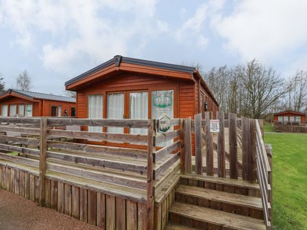 A wooden cabin with a fenced deck and stairs on a grassy area at Pegasus in Felmoor Park
