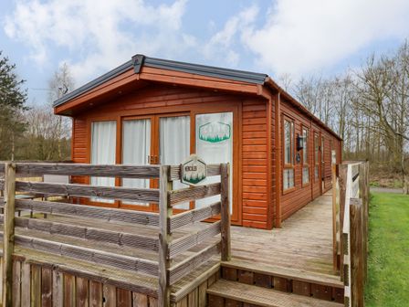 A wooden cabin with glass doors and windows and a wooden deck at Hercules in Felmoor Park