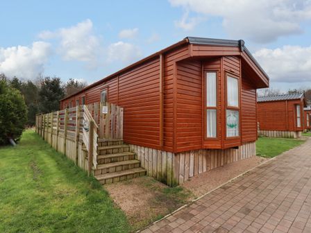 An outdoor view of a wooden cabin with a small staircase and a fenced porch at Canis in Felmoor Park