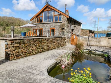 A stone house with large windows and a patio area next to a pond with plants at Monkleigh Mill Monkleigh near Bideford