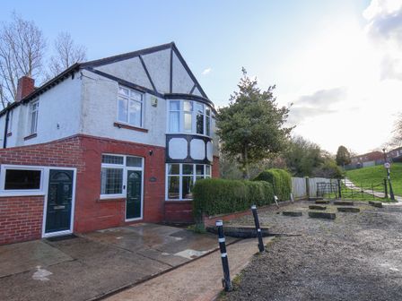 A semi detached house with bay windows and green doors next to a hedge and gravel area at Stakesby Villa Whitby