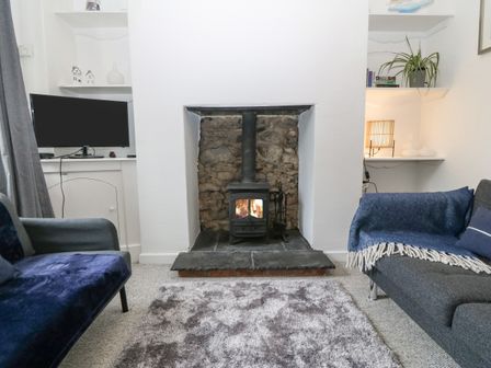 A living room with a wood burning stove and stone backdrop a television on a shelf and two sofas at Pebblestone Cottage in Llandudno