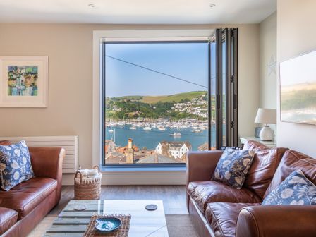 A living room with two leather sofas and a large window overlooking a harbor with boats and hills at 44 Above Town in Dartmouth