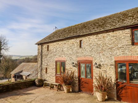 Exterior view of a stone building with wooden doors and windows and potted plants on a paved area at Bradley Stables in Withypool
