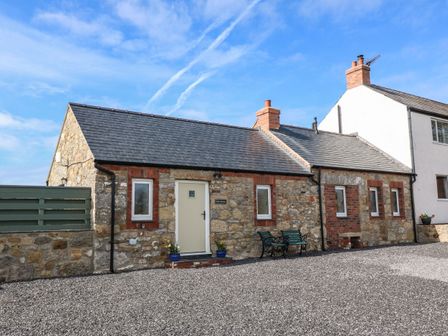 A stone cottage with a gravel yard and green bench at Pips Barn in Brynteg near Benllech