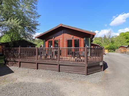 A wooden lodge with a fenced deck and outdoor furniture at Ghyll Lodge Grasmere 25 White Cross Bay Windermere