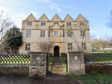 An old stone building with pointed roof peaks behind a metal gate and brick wall at Wick Court Farm in Arlingham near Frampton On Severn