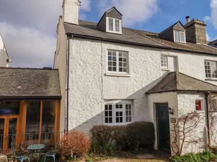 Exterior view of a white cottage with multiple windows and a black door with a small outdoor seating area at Early Mist Cottage in Haytor Vale