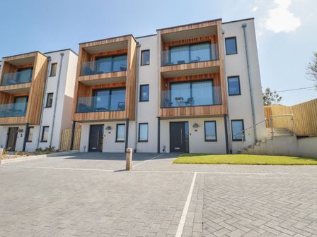 Modern townhouses with wooden framed balconies and glass railings with parking spaces and a grassy area at 7 Longshore in St Columb Minor