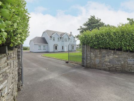 A two story house with a gated driveway and trimmed green hedges at Cloughoge House in Kilrush County Clare