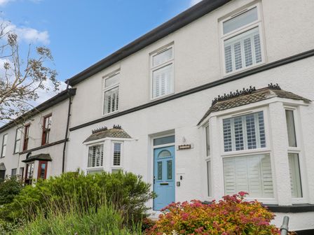 A row of white terraced houses with bay windows and a blue front door with plants in front at St Piran in Carbis Bay