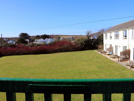 A grassy lawn with benches next to a white building and houses in the distance at Sky Pocket in Bude