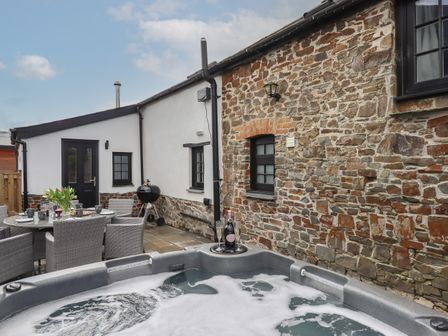 An outdoor patio with a hot tub champagne and glasses a dining table with chairs and a barbecue grill at Strawberry Bank - Pipistrelle in Bridgerule