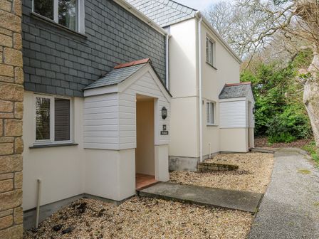 An exterior view of a building with two covered entrance porches a gravel path and surrounding trees at Woodmans Cottage in Falmouth