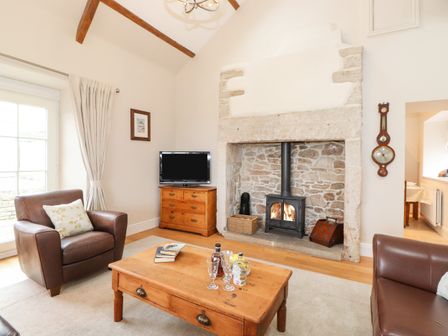 A living room with leather armchairs a wooden coffee table a stone fireplace and a television at Farnelea West Fleetham near Seahouses