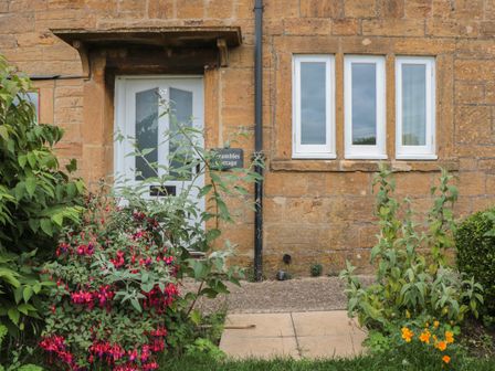 The front entrance door and windows of a stone building with plants and flowers in front at Scrambles Cottage in Stoke-Sub-Hamdon Somerset