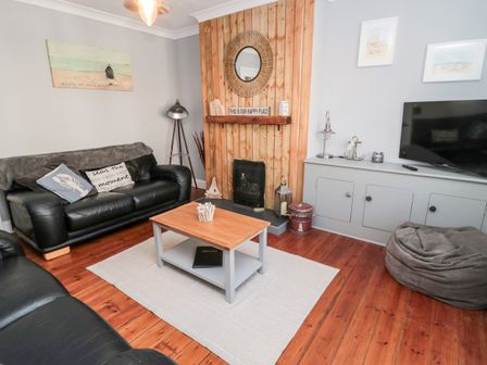 A living room with black leather sofas a wooden coffee table a fireplace with a round mirror and a television at 4 Percy Street in Amble