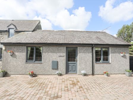 A grey stone building with two windows and a central door with potted flowers outside at Cae Ffynnon in Star near Gaerwen