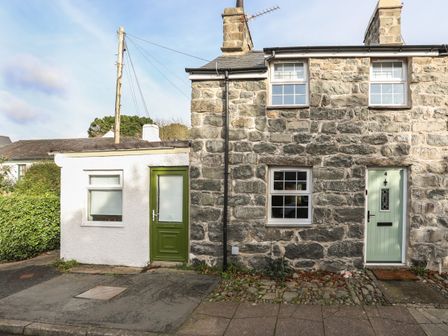 The front exterior of a stone house with mint green door and an attached white extension with a green door at Ty Eiddew Ivy House in Llanystumdwy near Criccieth