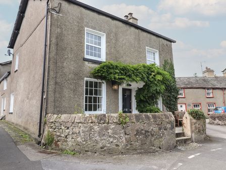 A stone house with white-framed windows and a black door surrounded by a stone wall at Caton Lane House in Cark In Cartmel
