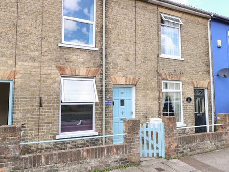 A brick terrace house with blue door and gate and windows showing curtains at Sole Bay Cottage in Lowestoft