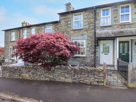 Stone terraced houses with white doors and red tree in front at Hannah's Cottage in Bowness-On-Windermere