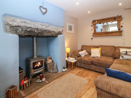 A living room with a wood burning stove in a blue alcove and a brown sectional sofa with cushions at Dolafon in Pwllheli