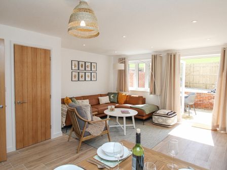 A living room with a brown sectional sofa armchair and round coffee table near a sliding door at Waterston Cottage in West Lulworth