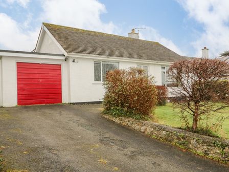 A white bungalow with a red garage door and shrubs in front at 5 Breeze Hill in Benllech