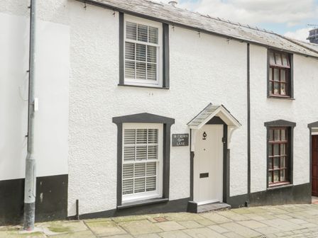 The front exterior of a white house with black trim and a white door on a cobblestone street at 14 Crown Lane in Conwy