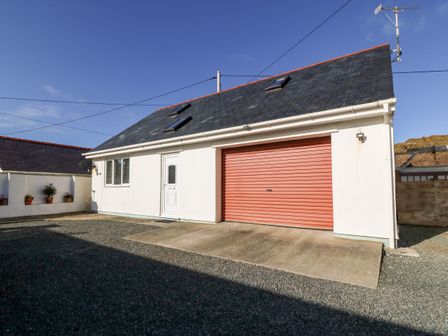 A white building with a red garage door and a white door under a dark slate roof with skylights at Glasfor Annex in Trearddur Bay