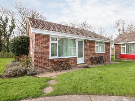A brick single-story house with two outdoor seating areas and grass lawn at 8 Royal Chalet Park in Mundesley