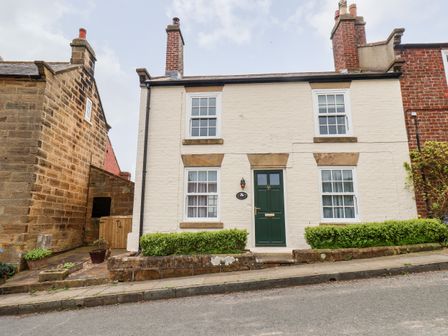 A white brick house with a green door and four windows on a sloped street at Braeside in Fylingthorpe