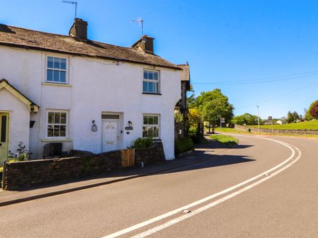 A white house with two chimneys next to a curved road under a blue sky at Meadow Cottage in Staveley