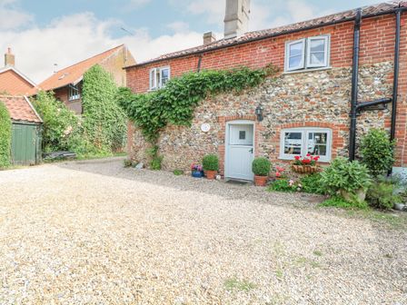 Exterior view of a stone and brick cottage with a blue door and windows surrounded by plants and gravel driveway at Cosy Cottage in Bawdeswell
