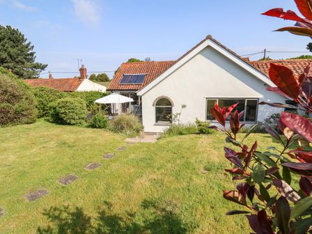 A house with a tiled roof and solar panels surrounded by a garden with bushes and grass at The Hollies in Westleton