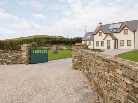 A gravel driveway leading to a two-story house with a stone wall and a green gate at Ballycahane in Castletownshend County Cork