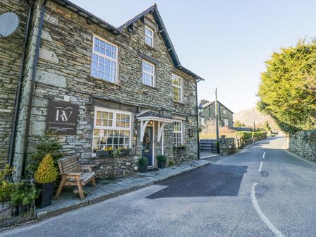 A stone building with windows and a bench on a small sidewalk beside a curved road at Raise View House in Grasmere