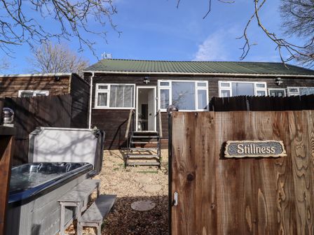 A backyard with a hot tub and a wooden fence with a sign reading Stillness at Stillness in Blandford Forum
